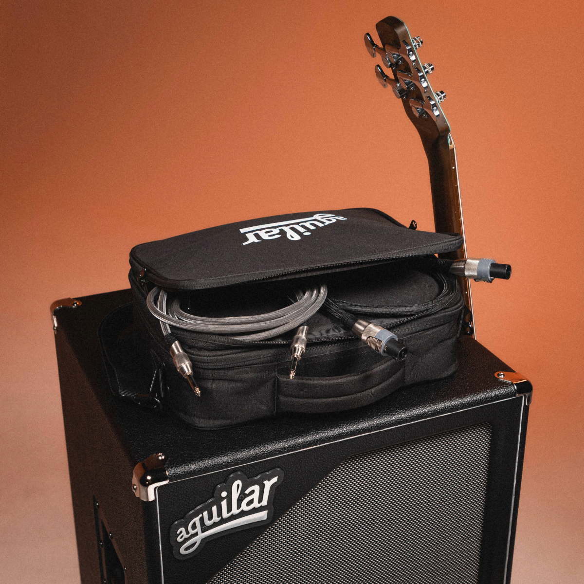 Guitar case with cables on a Aguilar amplifier against an orange background